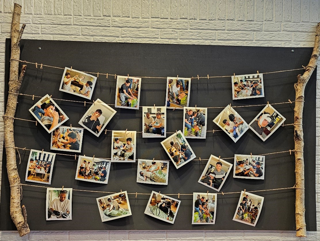 Fotowand mit quadratischen Fotos an Schnüren, an Wäscheklammern befestigt zwischen zwei Birkenstämmen vor weißer Ziegelwand