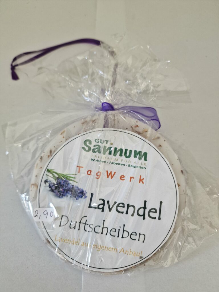 Runde Lavendel-Duftscheibe mit weißem Etikett und Lavendelbild, eingewickelt in durchsichtige Folie und mit violetter Schleife.