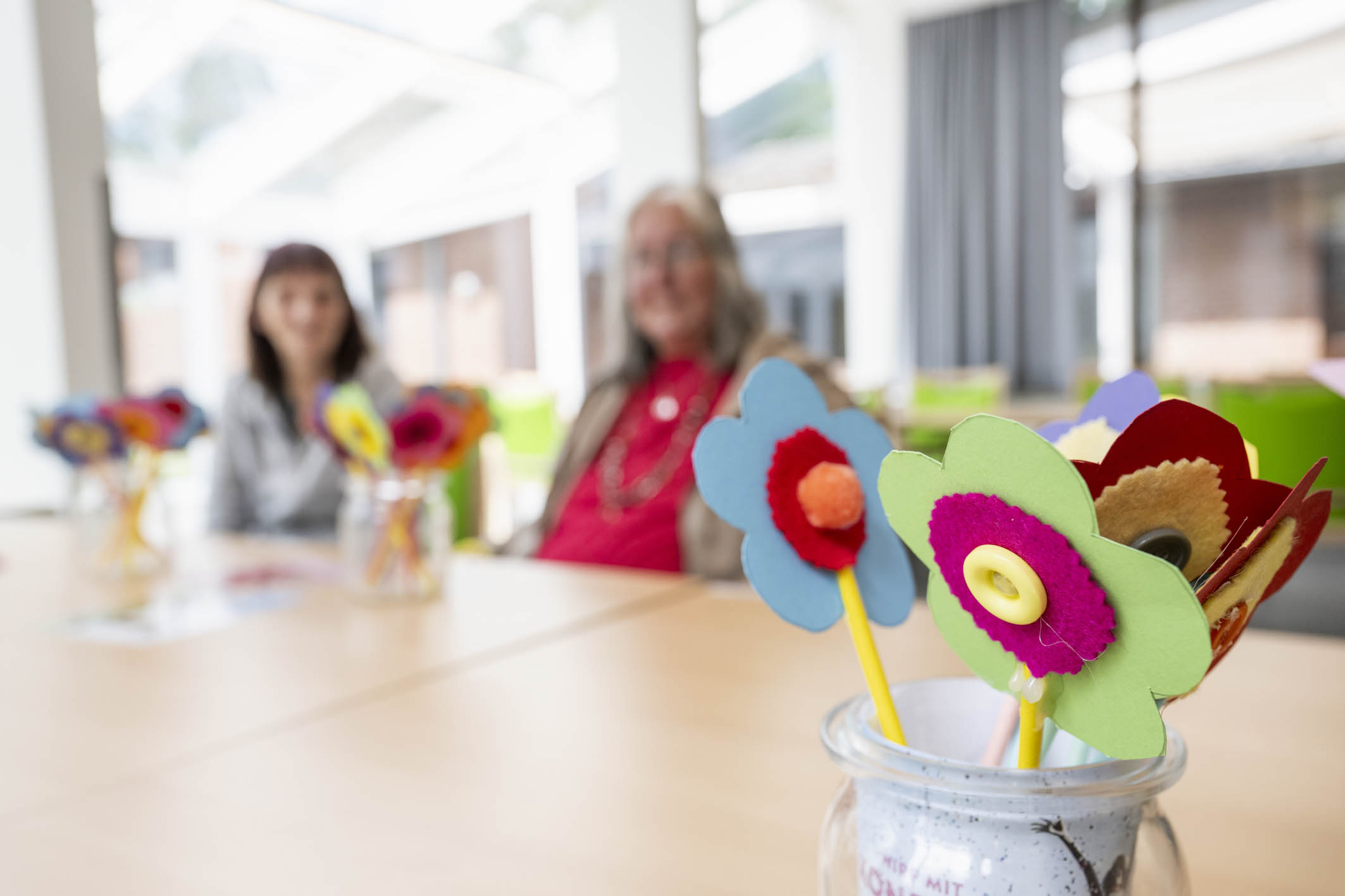 Zwei Pflegekräfte in roten Kasacks und weißen Hosen unterhalten sich und gehen vor einem Backsteingebäude entlang.