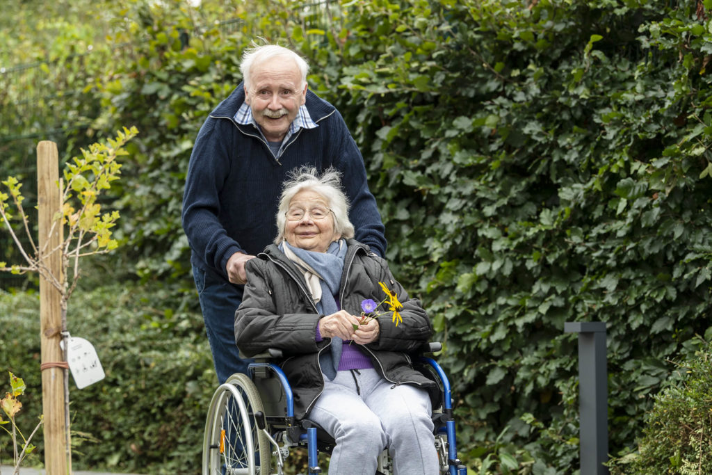 Ehemann schiebt seine Frau im Rollstuhl durch den Garten